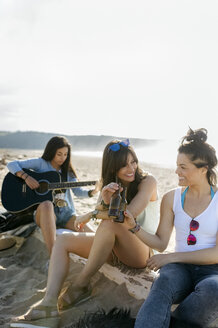 Junge Frau mit Freunden spielt Gitarre am Strand - MGOF04085