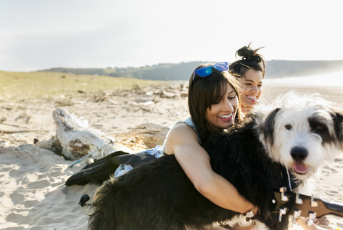 Zwei glückliche Frauen mit Hund am Strand, lizenzfreies Stockfoto
