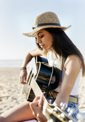 Junge Frau spielt Gitarre am Strand - MGOF04097