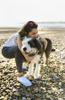 Junge Frau kuschelt mit Hund am Strand - MGOF04105