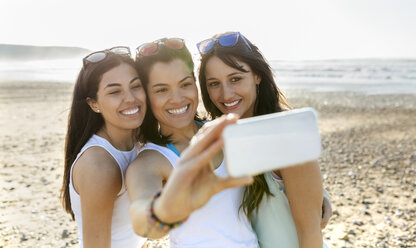 Portrait of happy female friends taking a selfie on the beach - MGOF04106