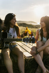 Zwei glückliche Frauen mit Gitarre und klirrenden Bierflaschen auf der Strandpromenade in den Dünen - MGOF04115