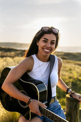 Portrait of a smiling young woman with guitar in dunes - MGOF04117