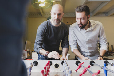 Colleagues playing foosball in office - FMOF00683