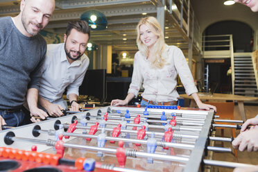 Happy colleagues playing foosball in office - FMOF00684