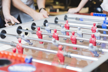 Close-up of colleagues playing foosball in office - FMOF00686