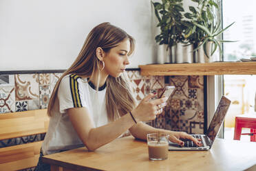 Junge Frau, die das Mobiltelefon und den Laptop im Café benutzt - ACPF00523