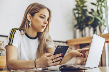 Young woman using mobile phone and laptop in cafe - ACPF00528