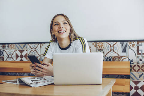 Junge Frau, die das Mobiltelefon und den Laptop im Café benutzt, lizenzfreies Stockfoto