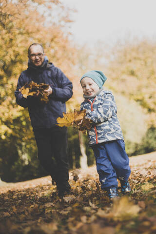 Glücklicher Vater und kleiner Sohn spielen mit Herbstblättern, lizenzfreies Stockfoto