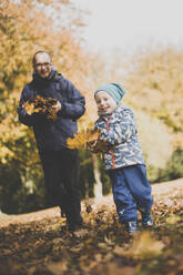 Glücklicher Vater und kleiner Sohn spielen mit Herbstblättern - IHF00099