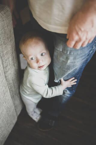 Ein kleines Mädchen versucht aufrecht zu stehen und hält die Jeans ihres Vaters, lizenzfreies Stockfoto