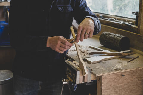 Bärtiger Mann mit schwarzer Mütze steht an einer Werkbank in einer Werkstatt und bearbeitet ein Stück Holz., lizenzfreies Stockfoto