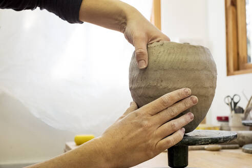 Close up of ceramic artist in her workshop, working on small clay vase. - MINF11330