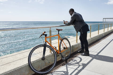 Mann mit Fahrrad auf der Uferpromenade, der sein Smartphone benutzt, lizenzfreies Stockfoto