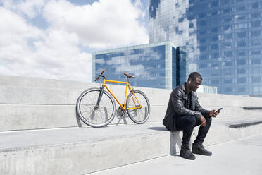 Mann mit gelbem Fahrrad, der auf einer Treppe sitzt und ein Smartphone benutzt, Barcelona, Spanien - JND00057