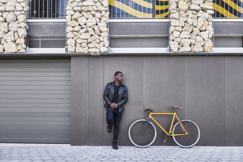 Mann lehnt neben seinem Fahrrad an einer Wand, lizenzfreies Stockfoto