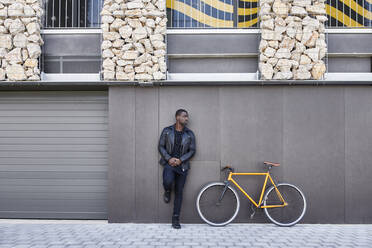 Mann lehnt neben seinem Fahrrad an einer Wand - JND00063