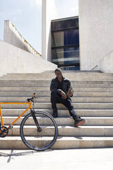 Mann macht ein Selfie, sitzt auf einer Stufe neben seinem Fahrrad - JND00071
