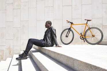 Mann sitzt auf einer Stufe neben seinem Fahrrad - JND00072