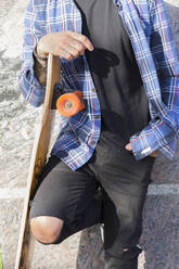 Tattooed young man with longboard leaning against wall, partial view - JPTF00130