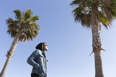 Junger Mann steht zwischen Palmen vor blauem Himmel - JPTF00132