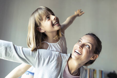 Mutter und Tochter spielen zu Hause und tun so, als würden sie fliegen, lizenzfreies Stockfoto