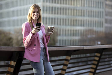 Young businesswoman using smartphone and holding coffee to go - JSRF00194