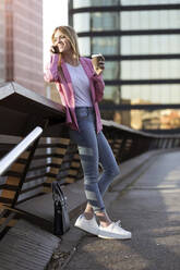 Young businesswoman using smartphone and holding coffee to go - JSRF00195