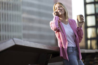 Young businesswoman using smartphone and holding coffee to go - JSRF00196