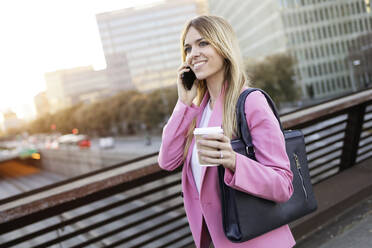 Young businesswoman using smartphone and holding coffee to go - JSRF00200