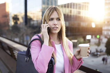 Young businesswoman using smartphone and holding coffee to go - JSRF00201