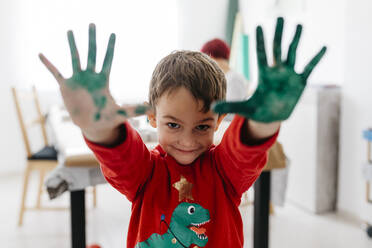 Boy showing his hands painted green while doing crafts at home - JRFF03251