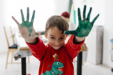 Junge zeigt seine grün bemalten Hände beim Basteln zu Hause - JRFF03251