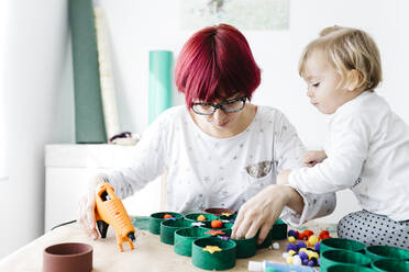 Mother and daughter doing crafts at home with accessories to make a Christmas tree - JRFF03265