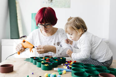 Mother and daughter doing crafts at home with accessories to make a Christmas tree - JRFF03266