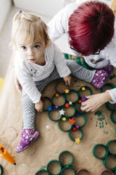Top view of mother and daughter doing crafts at home with accessories to make a Christmas tree - JRFF03272