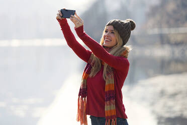 Junge blonde Frau macht ein Selfie an einem See im Winter - JSRF00207
