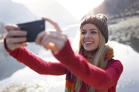 Junge blonde Frau macht ein Selfie an einem See im Winter, lizenzfreies Stockfoto