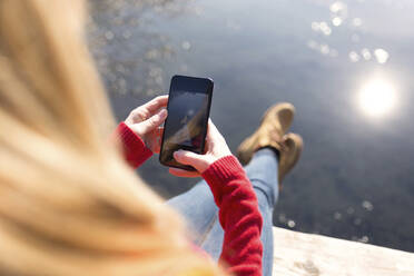 Young blond woman using smartphone at a lake in winter - JSRF00215