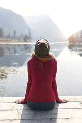 Junge blonde Frau sitzt auf einem Steg an einem See im Winter - JSRF00217