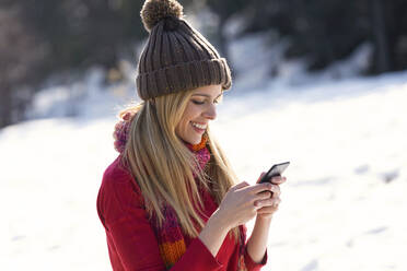 Junge blonde Frau benutzt Smartphone im Winter - JSRF00229