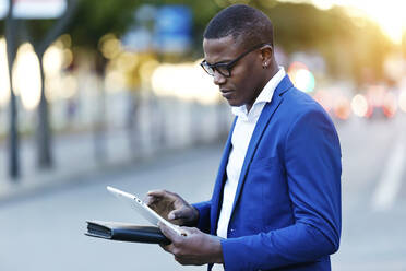 Young businessman wearing blue suit jacket and using his digital tablet at a street - JSRF00254