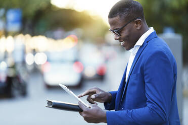 Junger Geschäftsmann in blauer Anzugsjacke, der sein digitales Tablet auf einer Straße benutzt - JSRF00255