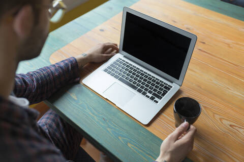 Man wearing pyjama sitting with coffee cup in front of laptop stock photo