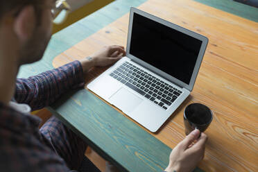 Mann im Pyjama sitzt mit Kaffeetasse vor einem Laptop - JPTF00150