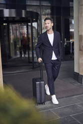 Mature man with trolley in front of a hotel - PNEF01594