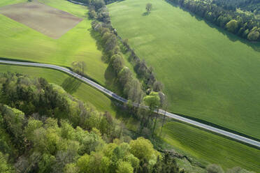 Luftaufnahme einer Landstraße durch eine Landschaft mit landwirtschaftlichen Feldern und Wald, Frühling, Franken, Bayern, Deutschland - RUEF02233