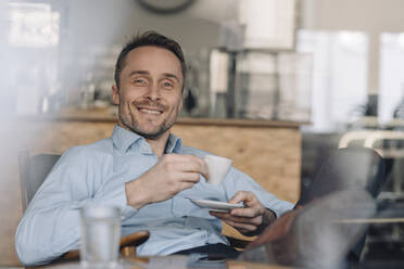 Successful businessman sitting in coffee shop, drinking coffee - KNSF06027