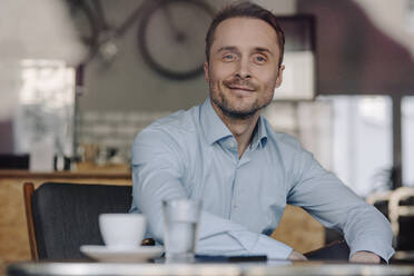 Successful businessman sitting in coffee shop, smiling, drinking coffee - KNSF06028